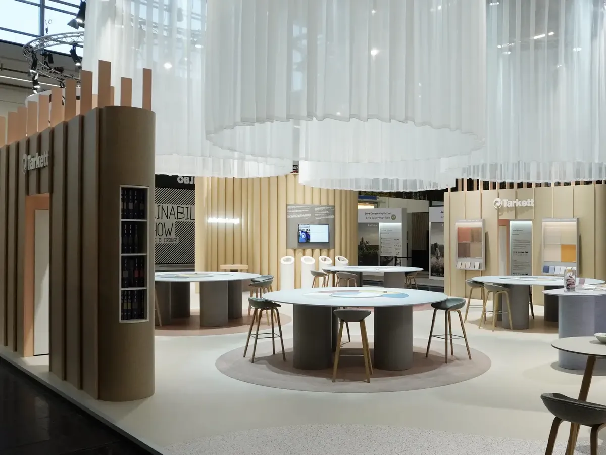 Tarkett stand with a white fabric ceiling installation, round consultation tables and cream-coloured slatted walls, presenting flooring solutions at BAU 2025