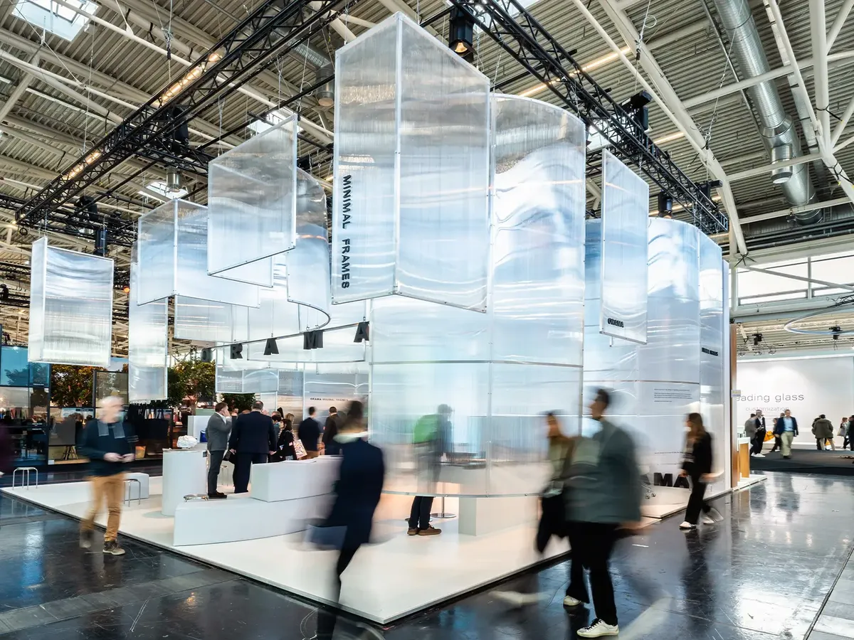 Orama Minimal Frames stand at BAU 2025 with floating, translucent panels above a white stand area, visitors moving in front of it