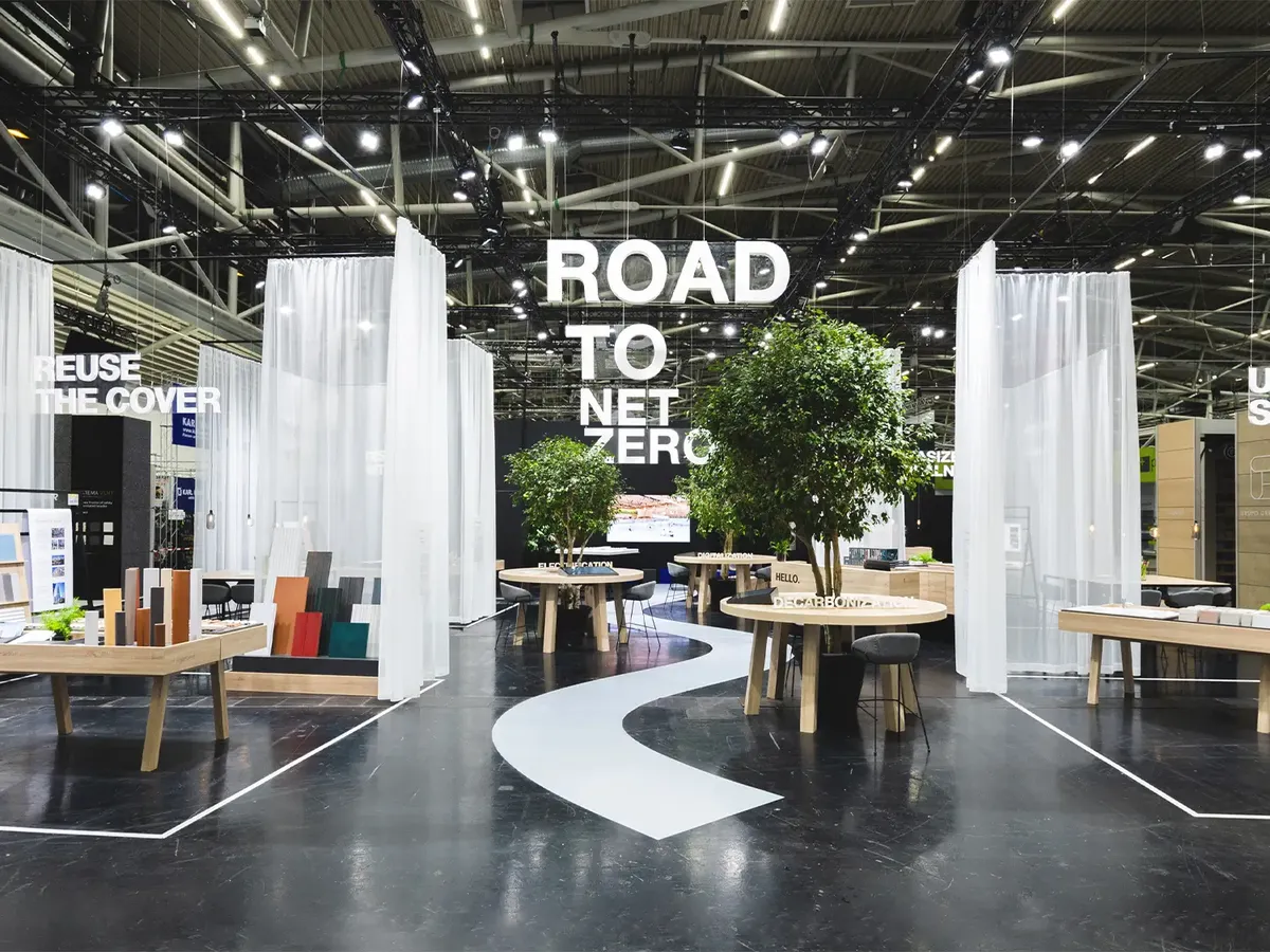 Agrob Buchtal stand with a curving white path line on a dark floor, visualising the »Road to Net Zero« claim. Open architecture with transparent curtains and consultation zones