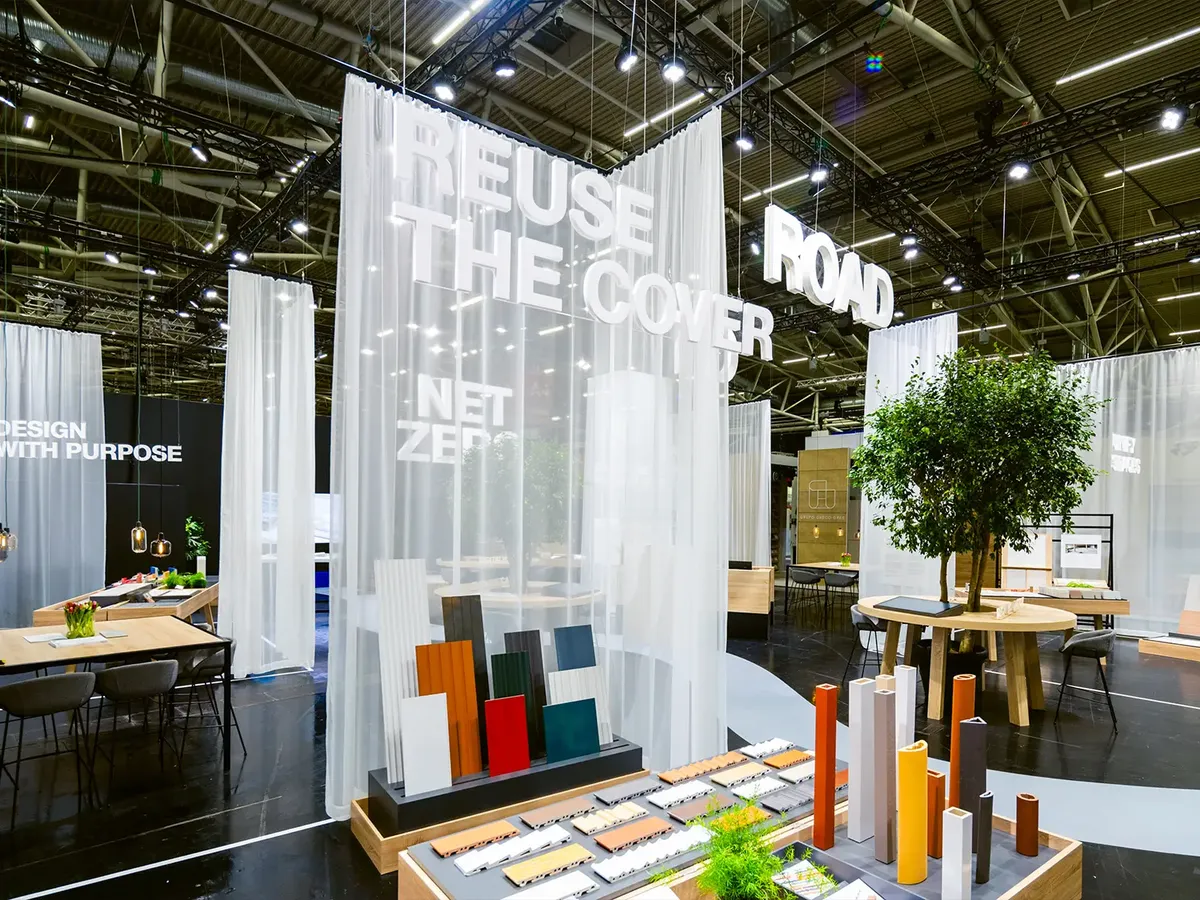 Stand with the »Reuse the Cover« motto, white curtains and a product presentation in earth tones, complemented by green plants and consultation tables at BAU 2025