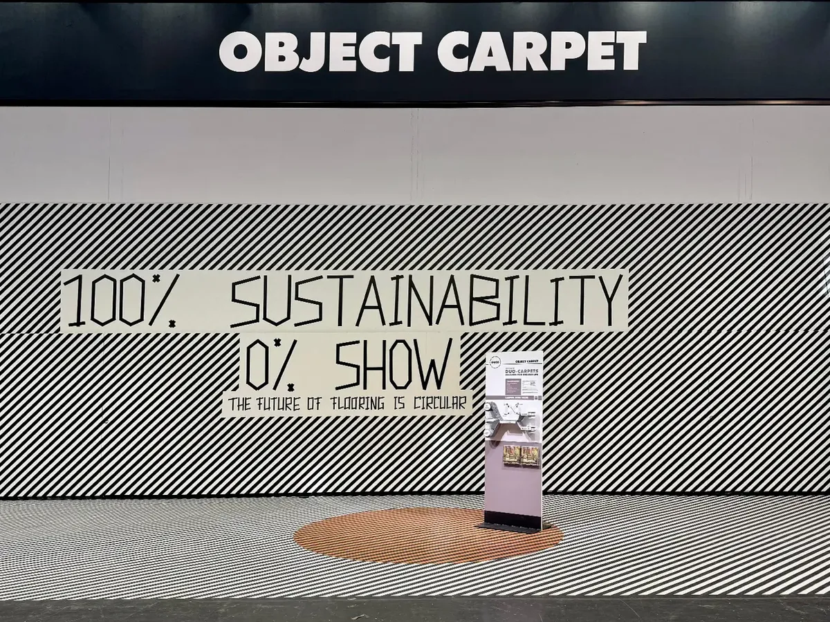 Object Carpet stand at BAU 2025 with the minimalist concept »100% Sustainability, 0% Show«. Black and white striped wall design with a clear statement on sustainability and a single product display on an orange circular detail.