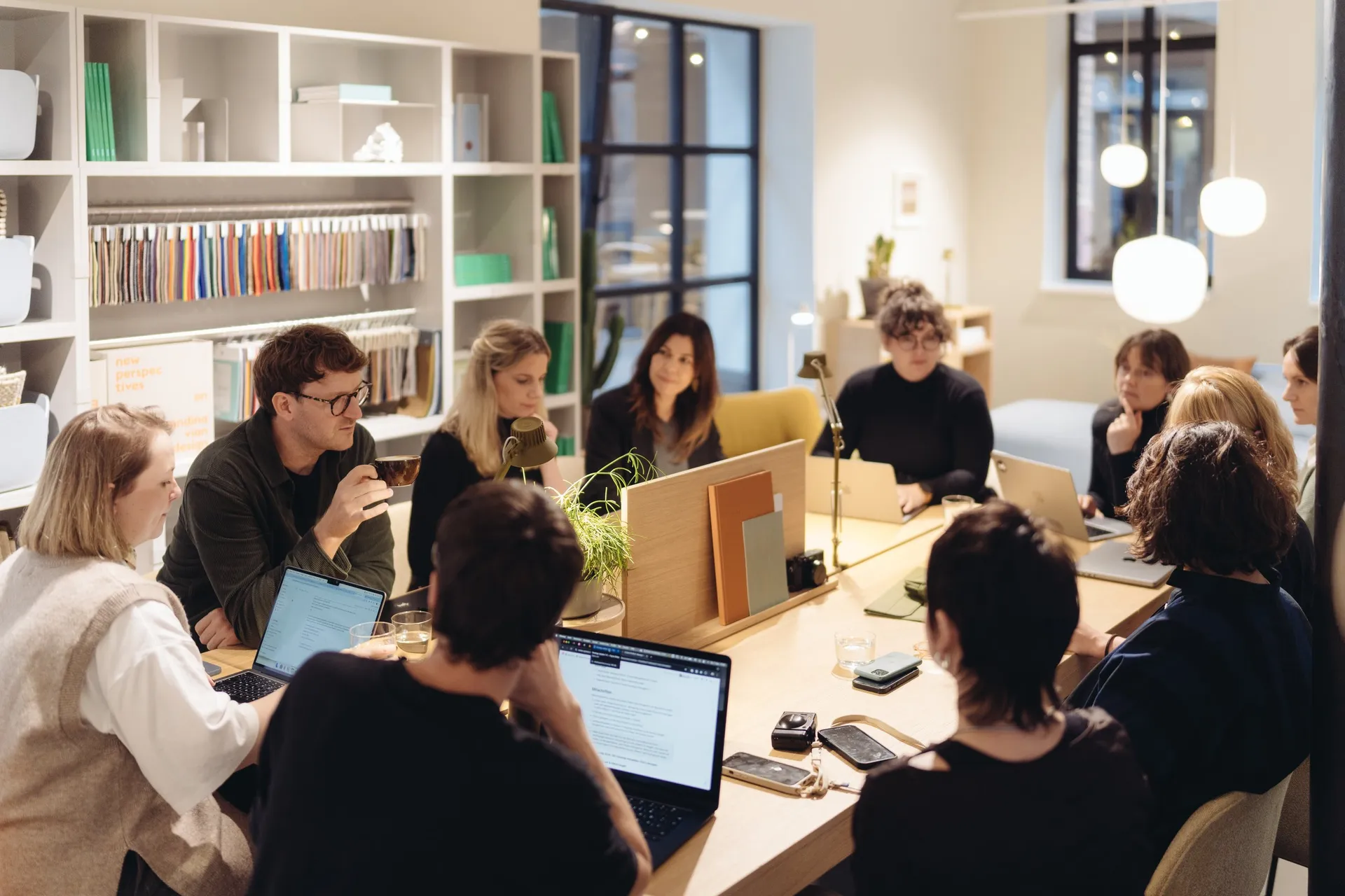 Workshop-Runde an einem langen Tisch in einem Showroom, mehrere Personen arbeiten an Laptops, im Hintergrund Bücherregale